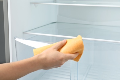 Woman cleaning empty refrigerator with rag, closeup