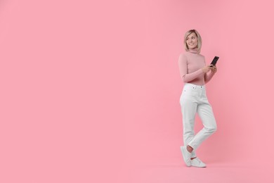 Photo of Happy woman with phone on pink background, space for text