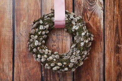 Wreath made of beautiful willow branches hanging on wooden background