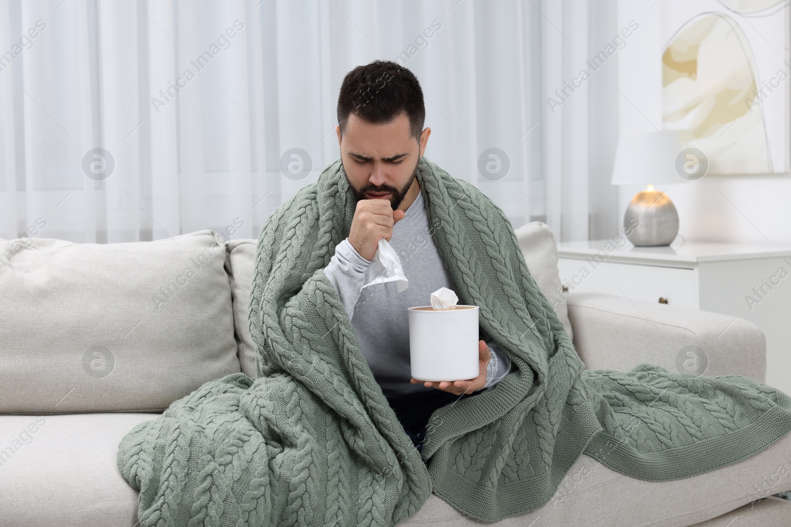 Photo of Sick man with tissue coughing at home