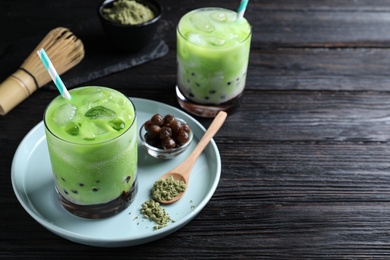 Photo of Tasty milk bubble tea with green matcha on black wooden table. Space for text