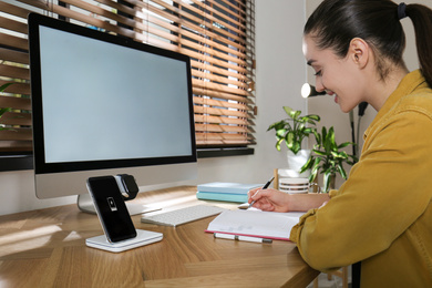 Photo of Woman at desk, smartphone and watch on wireless charger. Modern workplace