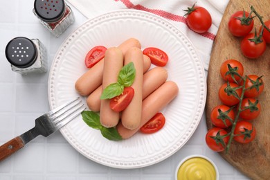 Photo of Delicious boiled sausages with tomatoes and basil served on white tiled table, flat lay