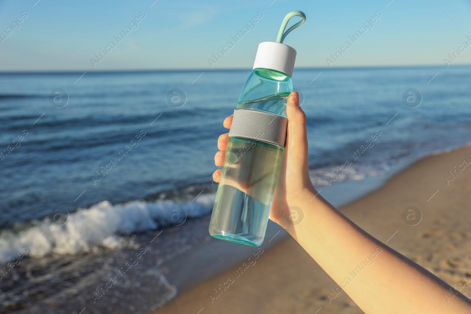 Photo of Woman holding glass bottle with water near sea, closeup