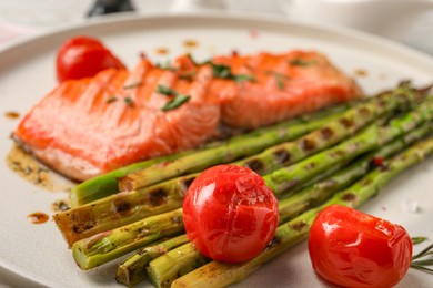 Tasty grilled asparagus, tomatoes and salmon on plate, closeup