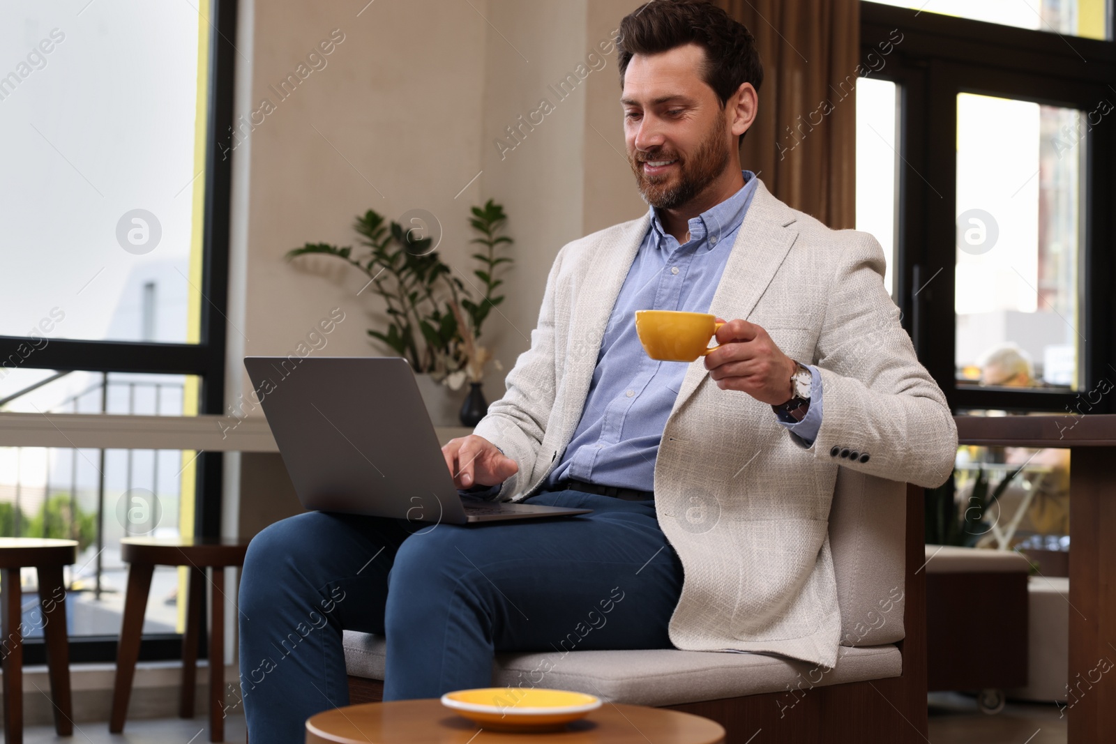 Photo of Man with cup of hot drink using laptop in cafe
