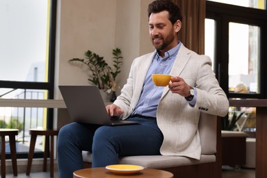 Photo of Man with cup of hot drink using laptop in cafe