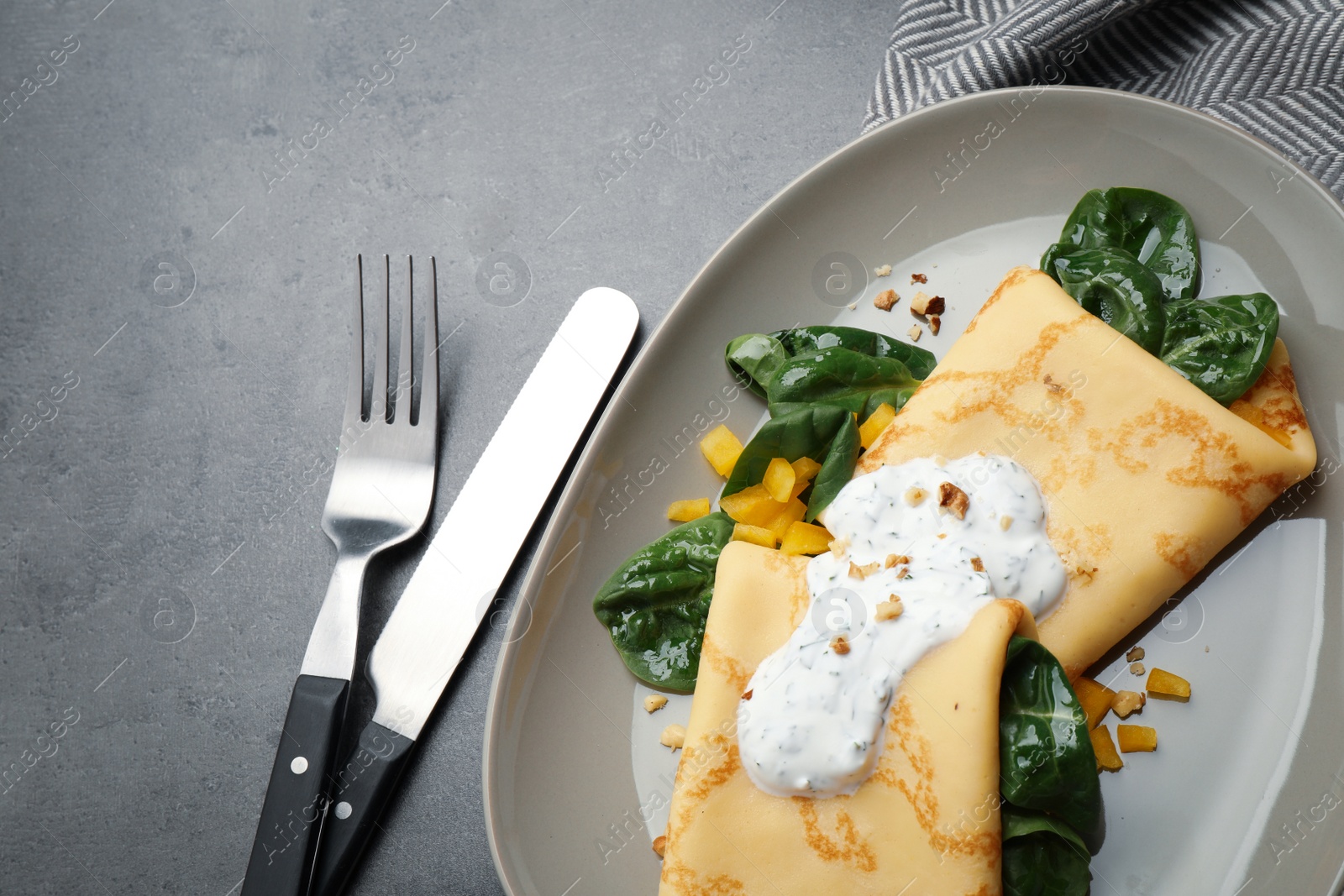 Photo of Delicious thin pancakes with spinach and sour cream on grey table, flat lay