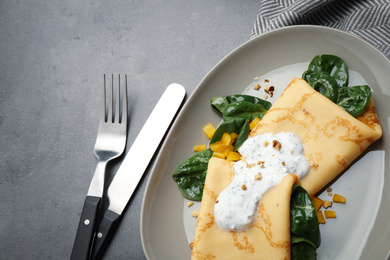 Photo of Delicious thin pancakes with spinach and sour cream on grey table, flat lay