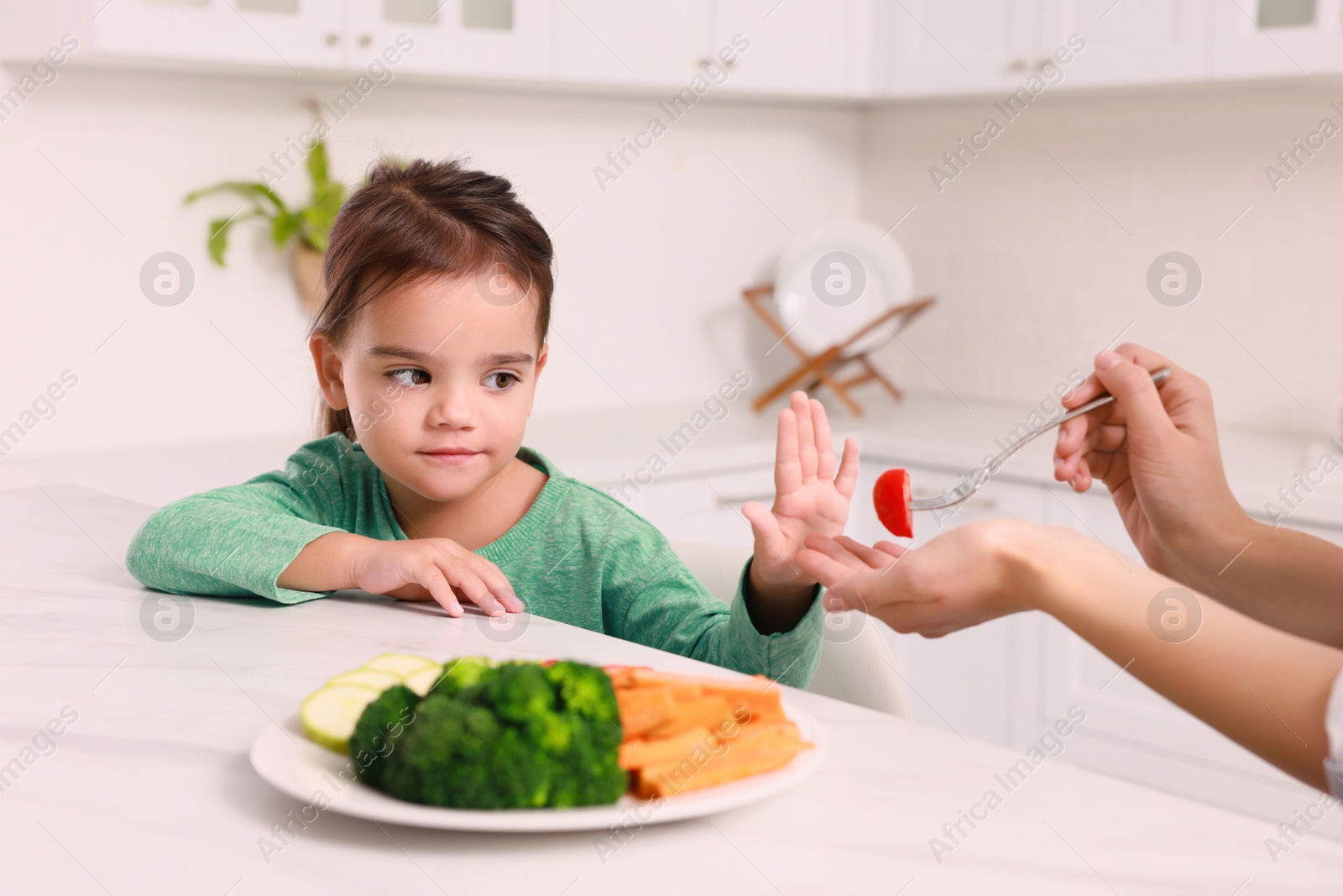 Photo of Mother feeding her daughter in kitchen, closeup. Little girl refusing to eat vegetables