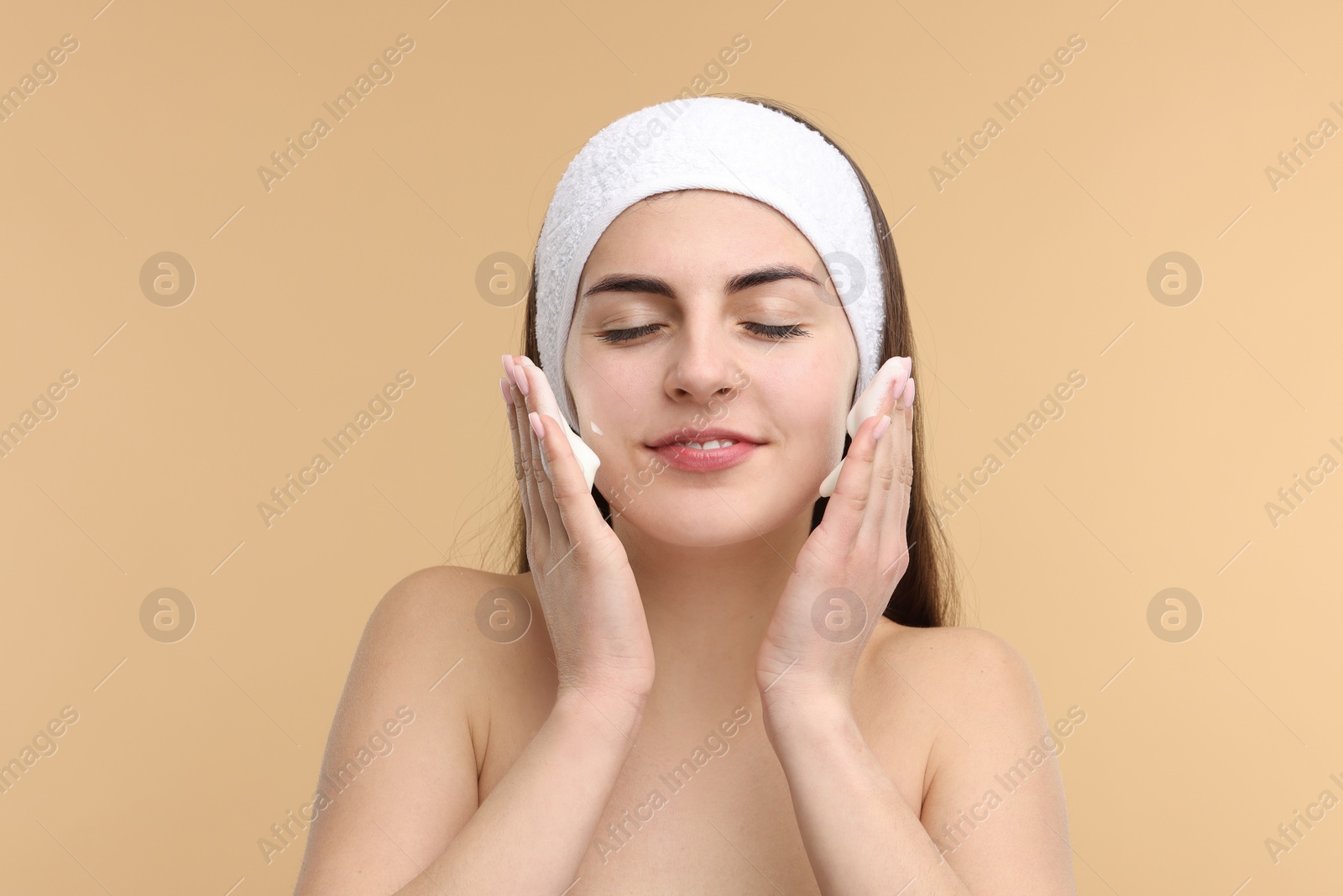 Photo of Young woman with headband washing her face on beige background