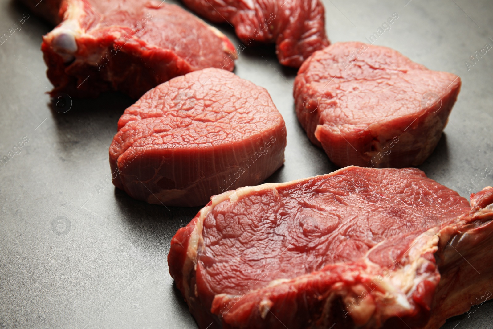 Photo of Fresh raw beef cuts on grey table, closeup