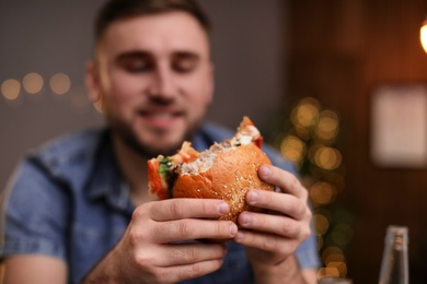 Young man eating tasty burger in cafe