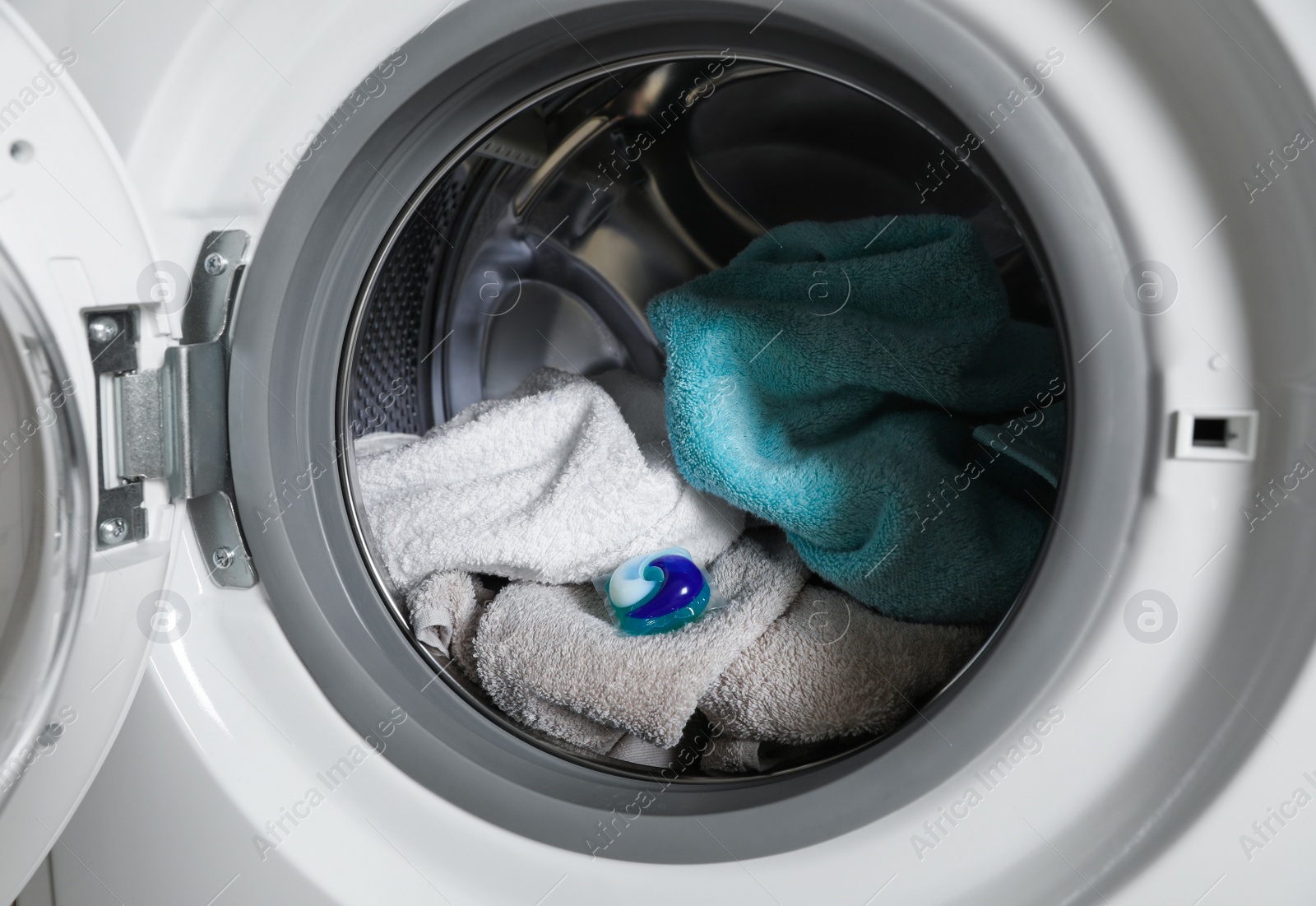 Photo of Laundry detergent capsule and towels in washing machine drum, closeup view