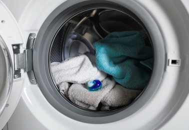 Laundry detergent capsule and towels in washing machine drum, closeup view