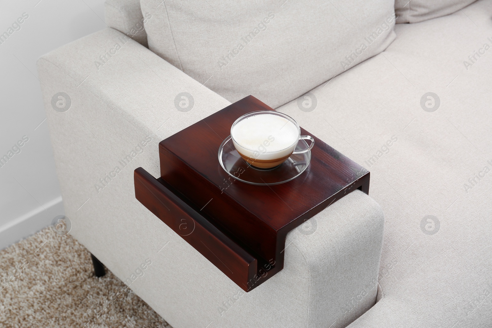 Photo of Cup of coffee on sofa with wooden armrest table indoors. Interior element