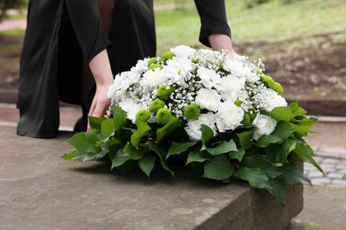 Photo of Woman with wreath of flowers near tombstone outdoors, closeup. Funeral attribute