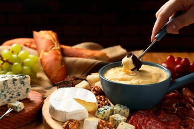 Photo of Woman dipping piece of bread into fondue pot with melted cheese at table, closeup