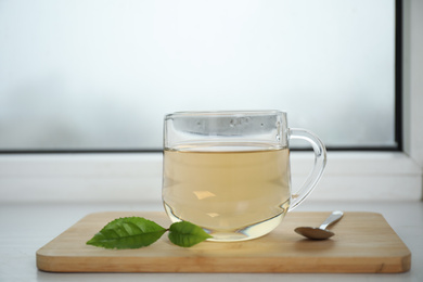 Photo of Tasty hot green tea in cup on window sill, closeup