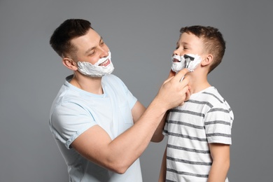 Dad pretending to shave his son with razor on grey background