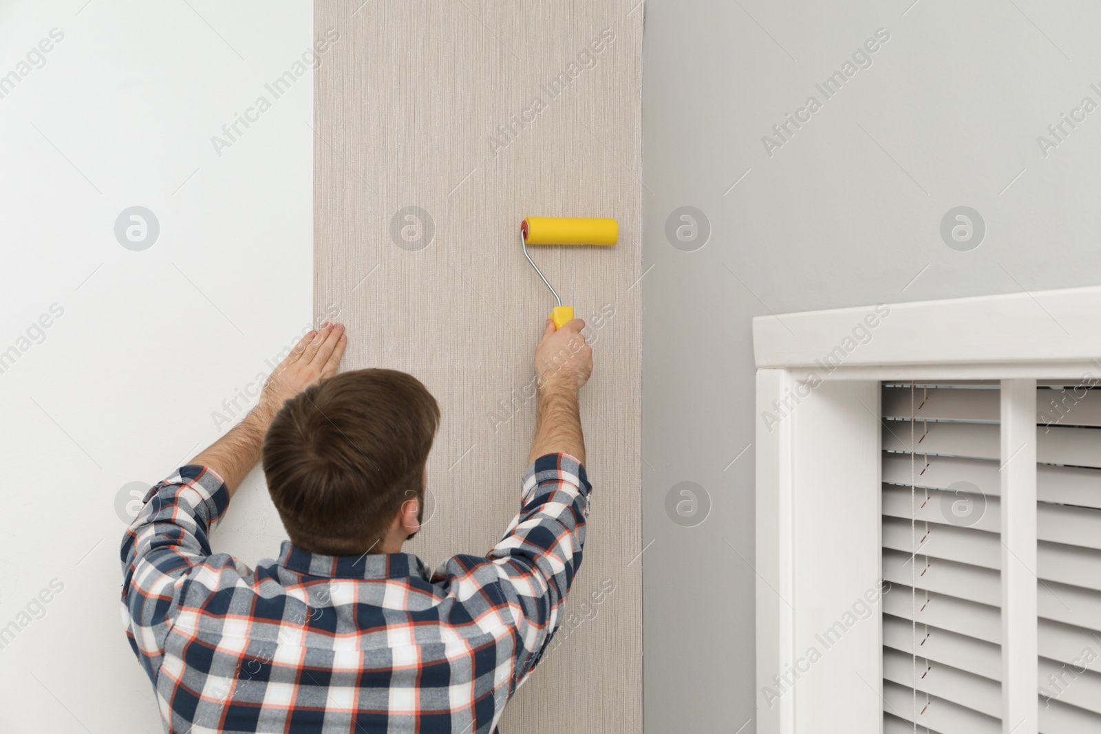 Photo of Man hanging stylish wall paper sheet indoors, back view