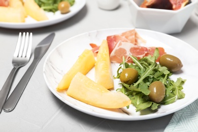 Photo of Plate with melon slices, prosciutto and olives on gray table