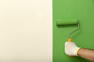 Man applying green paint with roller brush on white wall, closeup. Space for text
