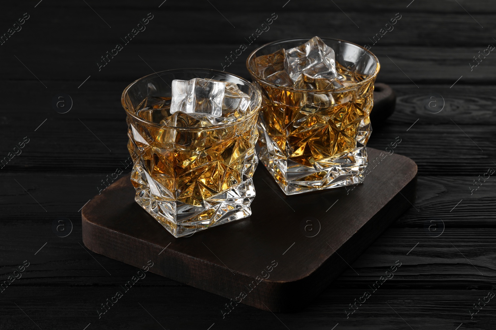 Photo of Whiskey and ice cubes in glasses on black wooden table, closeup