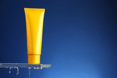 Photo of Moisturizing cream in tube on glass with water drops against blue background. Space for text
