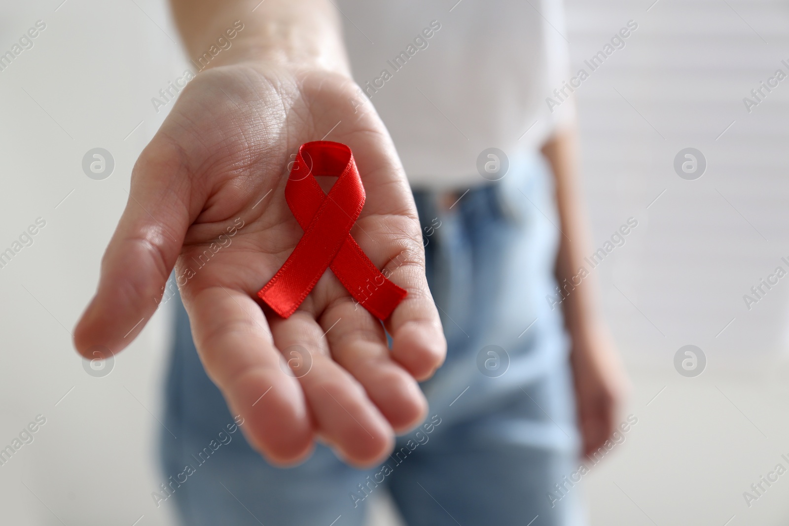 Photo of Woman holding red awareness ribbon on light background, closeup with space for text. World AIDS disease day