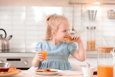 Photo of Adorable little girl eating tasty toasted bread with jam at table in kitchen