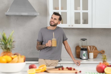 Photo of Handsome man with delicious smoothie in kitchen