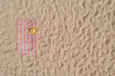 Image of Towel with straw hat on sandy beach, top view. Space for text