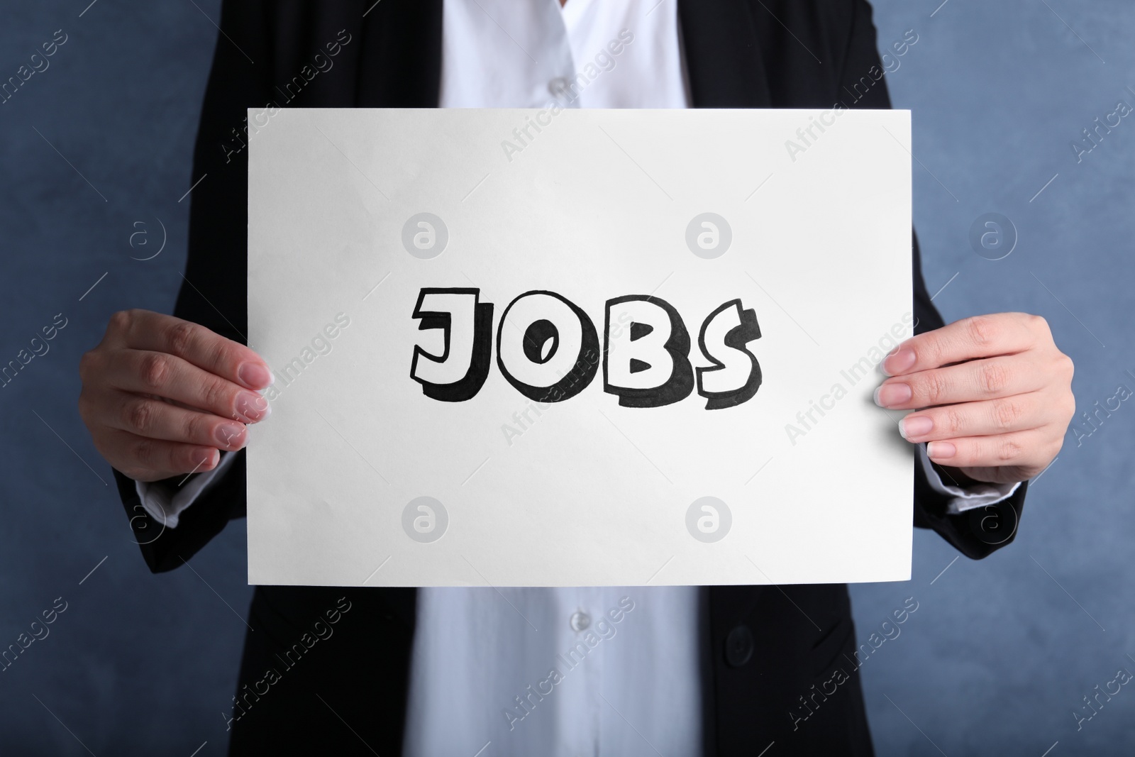 Photo of Woman holding sheet of paper with word JOBS on blue background, closeup. Career concept