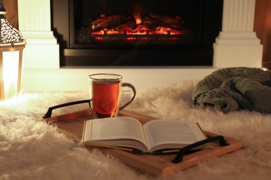 Cup of tea and book on fuzzy rug near fireplace at home. Cozy atmosphere