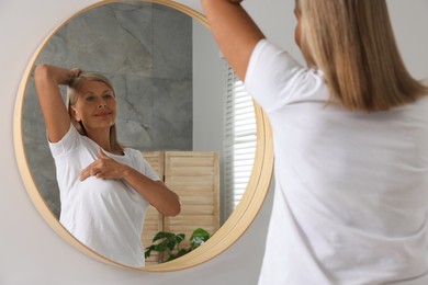 Photo of Beautiful senior woman doing breast self-examination near mirror in bathroom