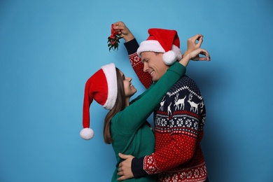 Happy couple standing under mistletoe bunch on light blue background