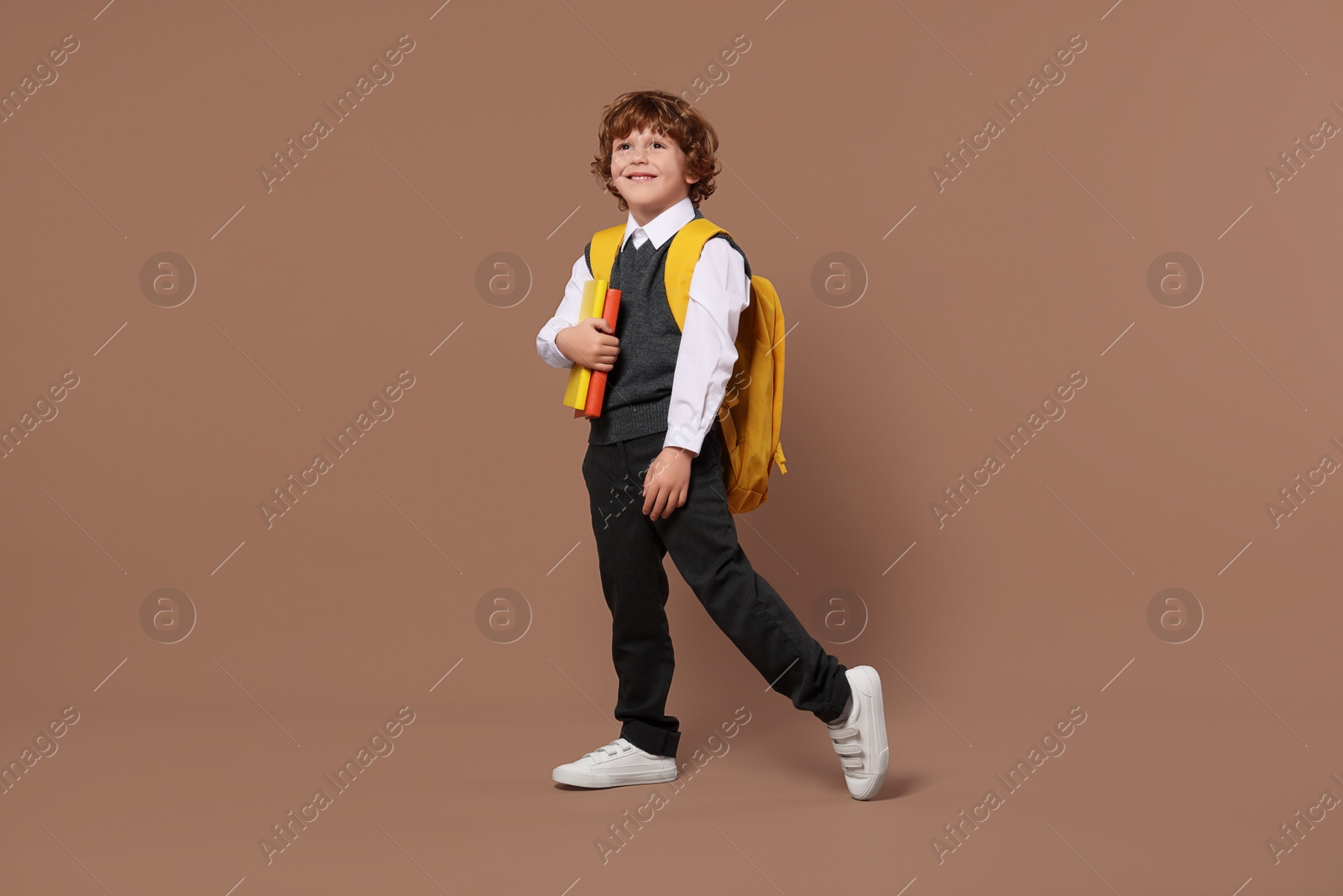 Photo of Happy schoolboy with backpack and books on brown background