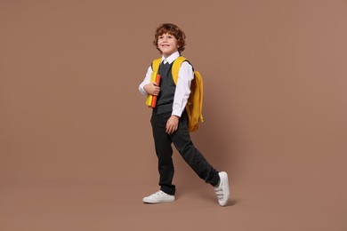 Happy schoolboy with backpack and books on brown background