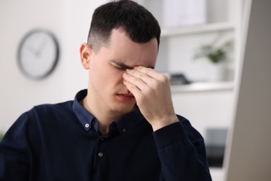 Young man suffering from headache in office, space for text