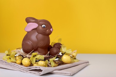 Beautiful composition with chocolate Easter bunny on white wooden table against yellow background. Space for text