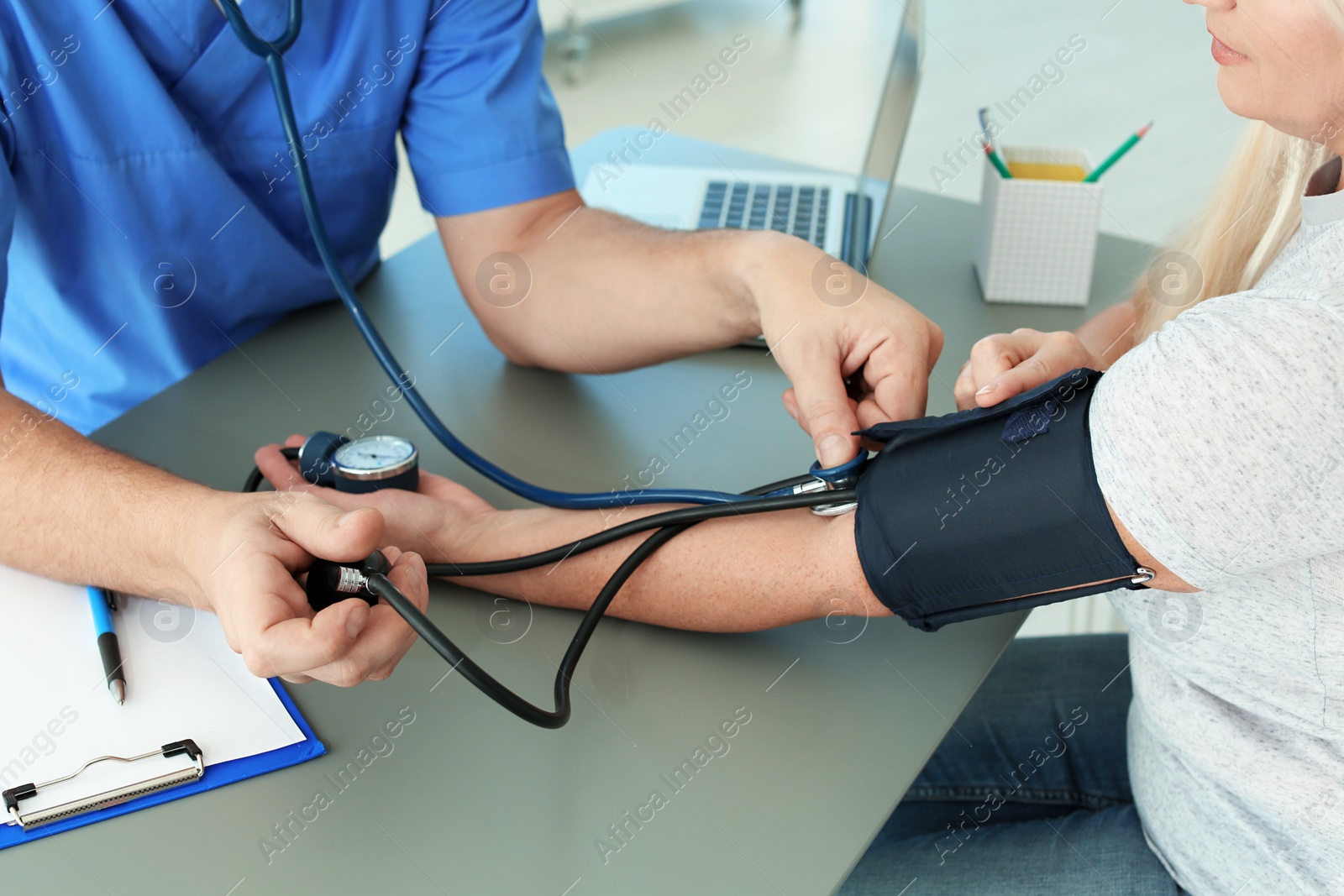 Photo of Close up view of medical assistant measuring female patient blood pressure in clinic
