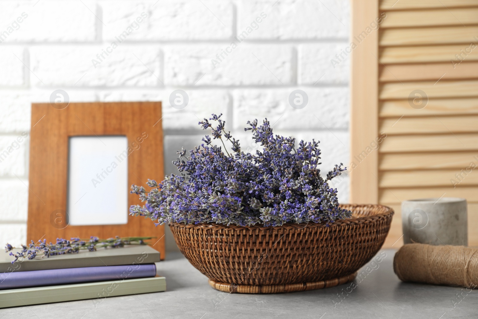 Photo of Composition with basket of fresh lavender flowers on stone table against white brick wall, space for text