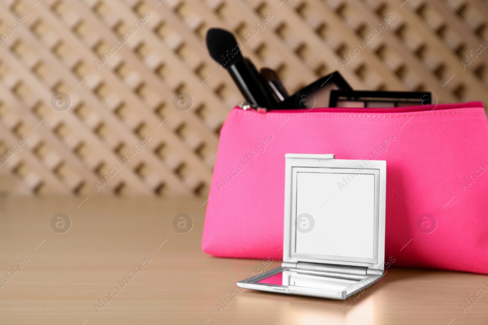 Photo of Stylish pocket mirror and cosmetic bag with makeup products on wooden table, space for text