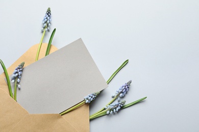 Envelope with beautiful spring muscari flowers and card on light background, flat lay. Space for text