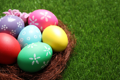 Photo of Colorful Easter eggs in decorative nest on green grass, closeup. Space for text