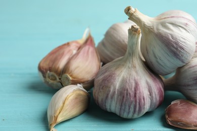 Photo of Fresh unpeeled garlic bulbs and cloves on light blue wooden table, closeup. Organic product