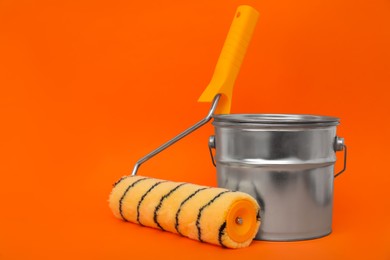 Photo of Can of orange paint and roller brush on color background. Space for text