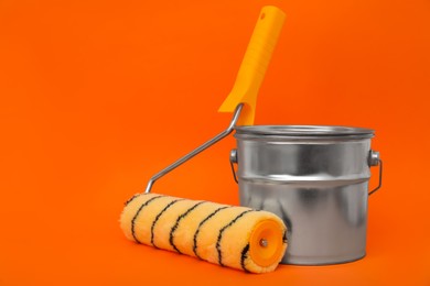 Can of orange paint and roller brush on color background. Space for text