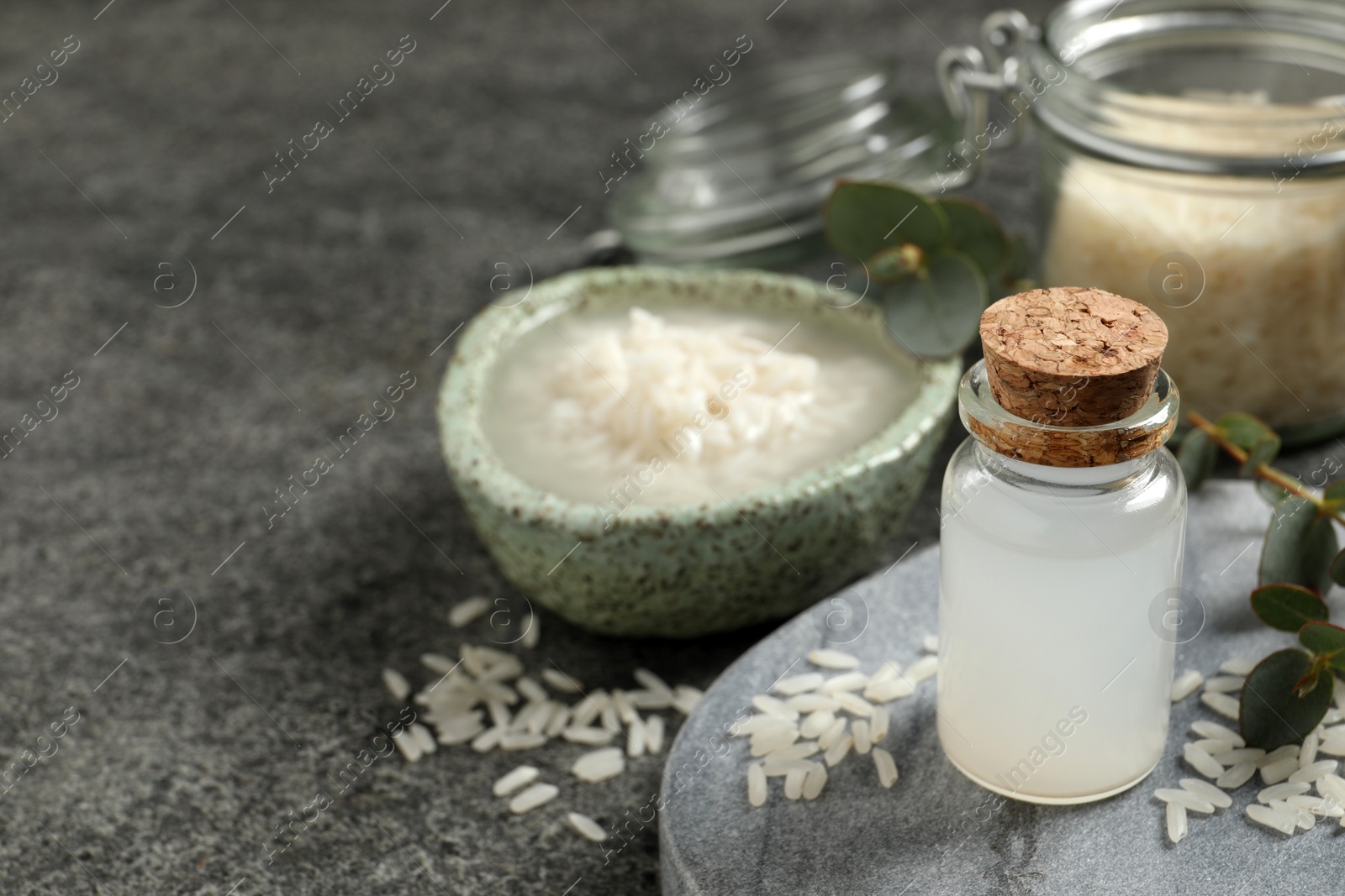 Photo of Glass bottle with rice water and grains on grey table. Space for text